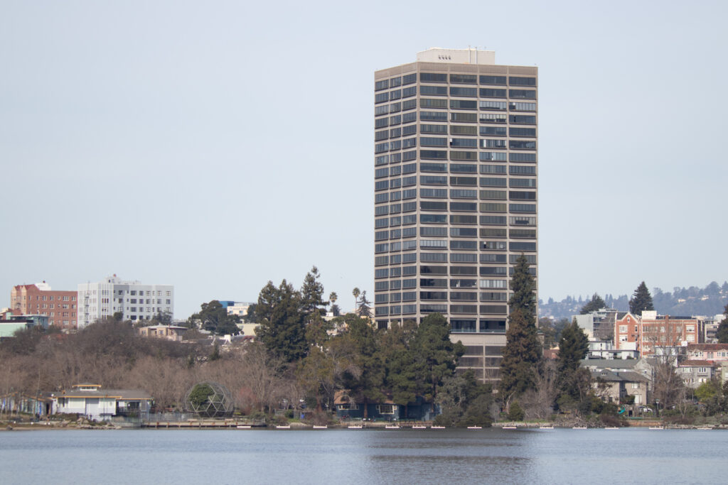 a photograph of Lake Merritt in Oakland, California, featuring buildings in the distance, a bird conservatory and trees in the middle distance, and the lake in the foreground