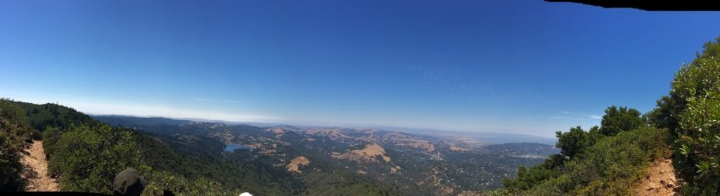 A panoramic shot from the top of Mount Tamalpais in Marin County, California. A hiking trail is visible on either end, and the land extends infinitely into the distance in the middle of the photograph.