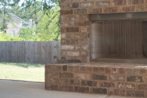 a color photograph of an outdoor fireplace in daytime, currently unused. a squirrel is laying flat on the fireplace, but its head has perked up to look behind it.