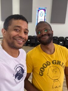 a color selfie of Mestre Malandro & David Brothers. Malandro is wearing a white shirt with a Filhos de Bimba logo. David is wearing a Peanuts shirt that features Charlie Brown saying, "Good grief."