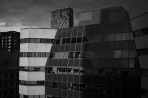 a black and white photograph of tall buildings in Montreal. One building, seen at an angle, is bright white. Next to it is a building seen face-on, but half covered by shadow.